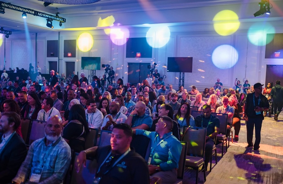 crowd of people sitting in chairs at an event with colorful lights all around them.