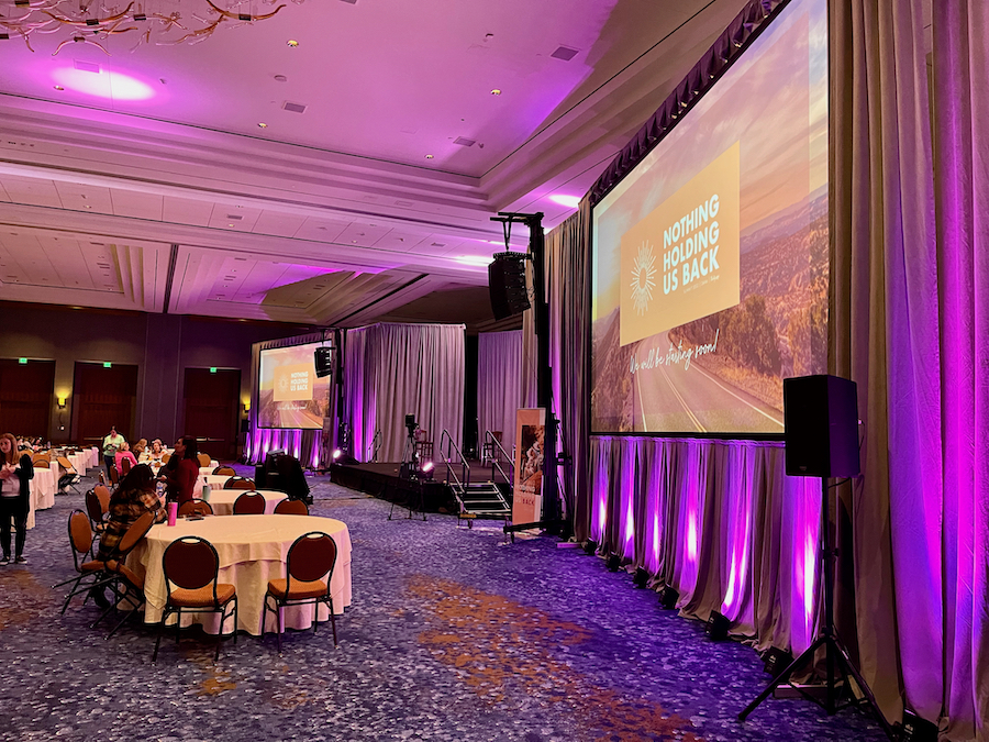 A hotel ballroom rental with a projector screen and purple lighting set for an event.