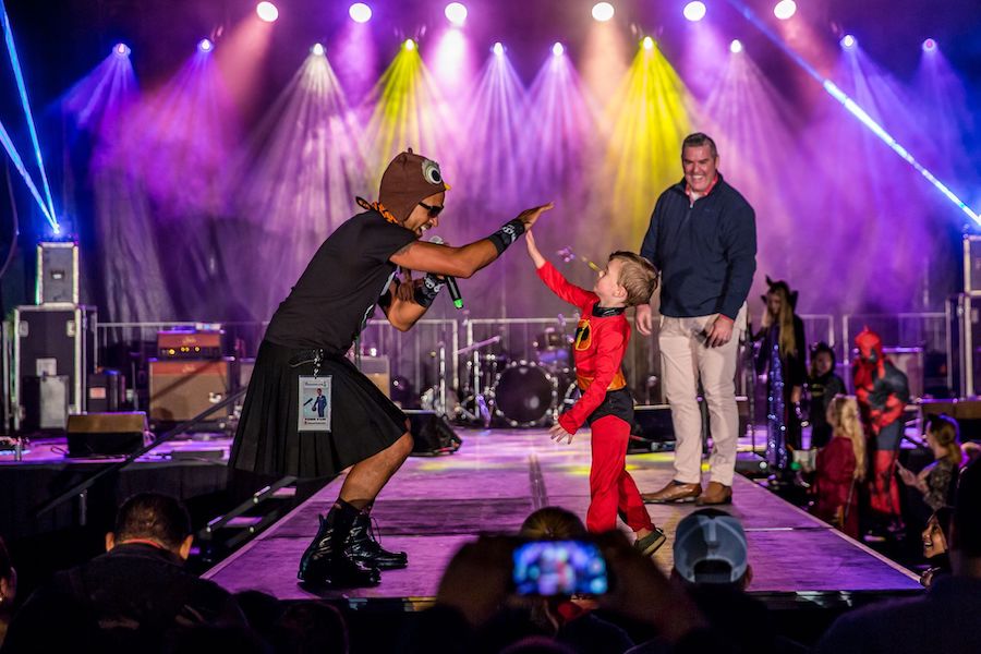 Child in costume high-fiving performer on a vividly lit concert stage.