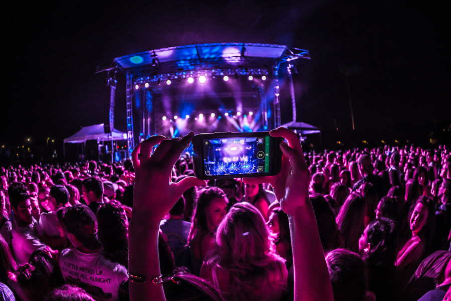 Someone holding up their phone to record a concert stage in the middle of a crowd.