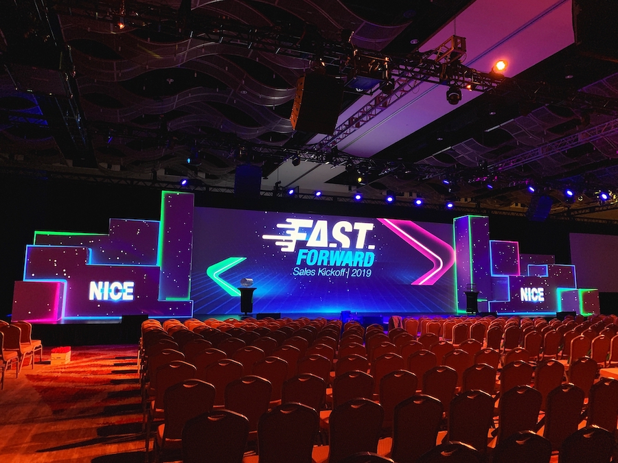 An auditorium with video walls on stage that read “Fast Forward Sales Kickoff” and “Nice.”