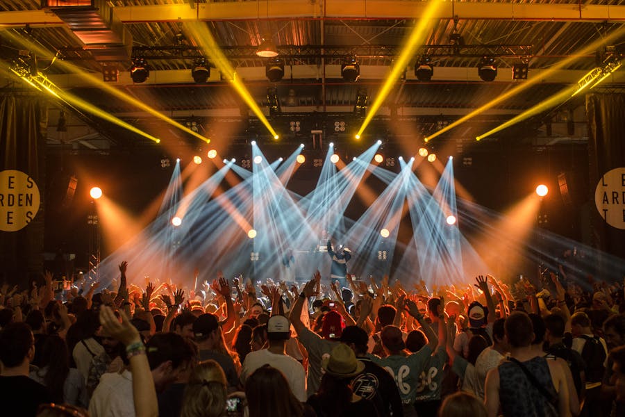 A group of people watching a concert where the stage is illuminated in white and orange hues.