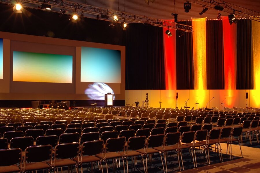 An auditorium hosting an event with various audiovisuals on stage.