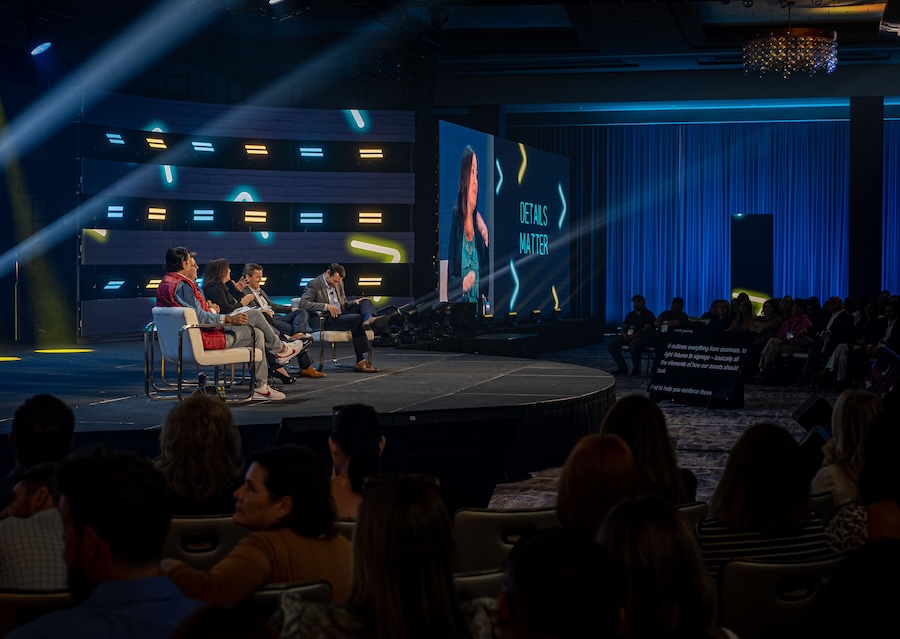Event guest speakers sit on a stage designed with a colorful, dynamic digital background
