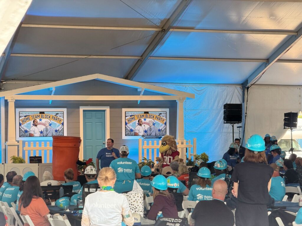 Man speaking with microphone in front of group of people in hard hats at the 40th Carter Work Project